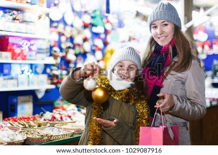 Woman and her daughter are shopping befor Christmas and showing balls on the tree outdoor.