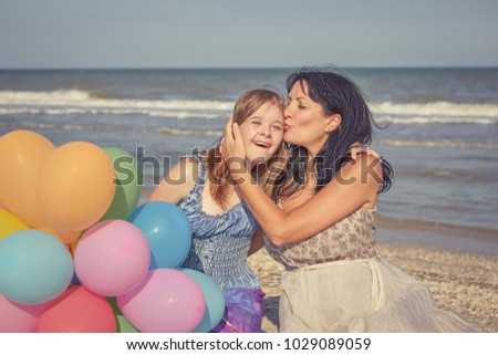 Happy family. Loving mother with seventeen-year-old daughter with Down syndrome on the beach With balloons. Positive human emotions, feelings.