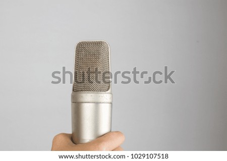 A hand holds condenser microphone for  recording isolated white background.