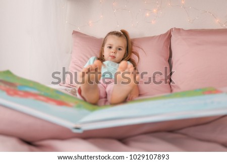 Cute little girl with book resting on bed at home