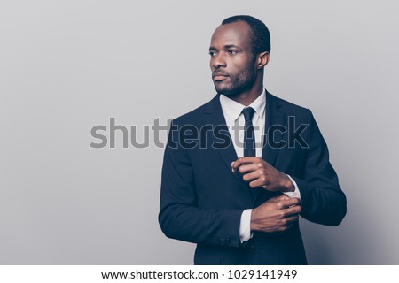 Portrait of stunning, trendy, attractive, dreamy, perfect man in black suit with tie fasten button on sleeve cuffs of white shirt, looking to the side, isolated on grey background Royalty-Free Stock Photo #1029141949