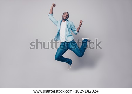 Portrait of flying, crazy, carefree, free, cheerful, funny man in sneakers, denim outfit, jumping with raised arms, celebrating victory, having fun, rest, relax, leisure, isolated on grey background Royalty-Free Stock Photo #1029142024