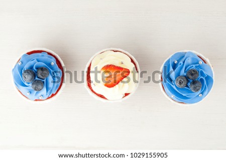 Cupcakes red velvet with blue and white whipped cream decorated with blueberry, strawberry on white wood table. Picture for a menu or a confectionery catalog. Top view.