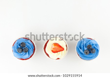 Cupcakes red velvet with blue and white whipped cream decorated with blueberry, strawberry on white background. Picture for a menu or a confectionery catalog. Top view.