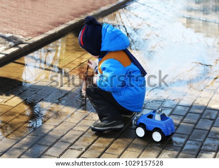 The spring children's play outdoors.The child squatting near a large puddle. Child is digging with a stick the water.