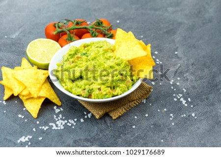 Avocado dip guacamole with tortilla chips in a white bowl on a black stone table. Traditional Mexican appetizer.