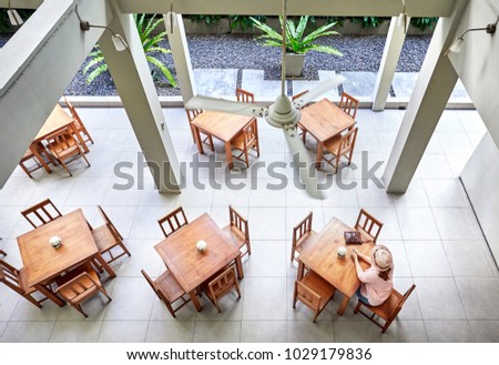 Woman in pink shirt and hat sitting at the table in hotel restaurant. Aerial view. 