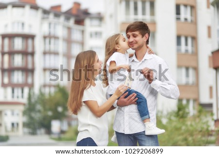 Shot of a happy young family posing together in front of new apartment building. Little girl kissing her father.Young woman posing with her daughter and husband in front of a new apartment building