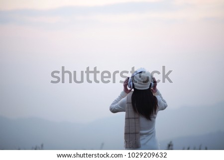 Rear view of young woman enjoying holding headphones listening to music and looking fog on the beautiful fog mountain happy and enjoy with vacation, on blurred fog background, Copy space,