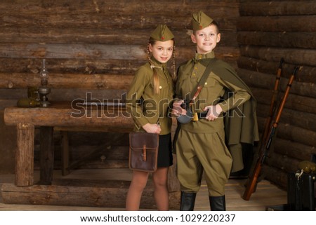 couple children in the old-fashioned Soviet military uniform with a binoculars on the background of a dugout from the bars