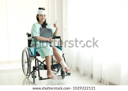 Young woman in hospital wheel chair. Happy smile as she got insurance money cover. Beautiful chinese woman. Medical, health insurance concept. Royalty-Free Stock Photo #1029222121