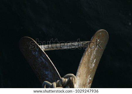 Top down photo of a plough shaped anchor on the bow of a sailboat against a dark watery background.
