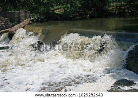 WATER RUSHING OVER A WIER CAUSING A WHITE CASCADE
