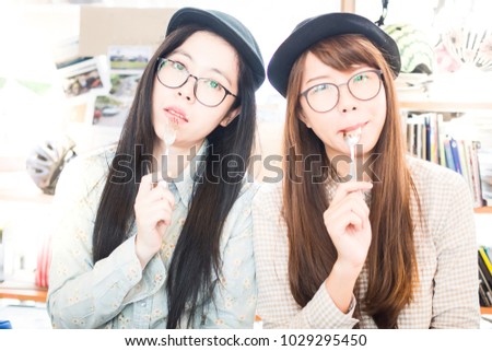 Two Happy Young Asian Girls with glasses and funny faces eating cake in cafe, having fun, and licking stain on lip and spoon. Concept of Best Friends hang out having good time together in coffee shop