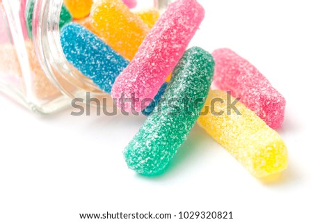 closeup of traditional acidulated candies faling from glass container on white background 