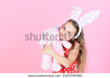 Happy girl hugging rabbit toy on pink background. Childhood, youth and growth. Fertility and new life concept. Child smiling with bunny ears headband. Easter and spring celebration, copy space