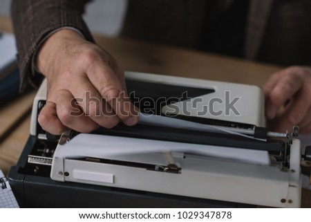 cropped shot of writer loading paper into typewriter