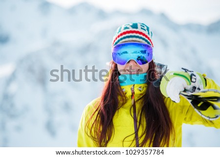 Image of woman in mask with skis on her shoulder against snowy hill background