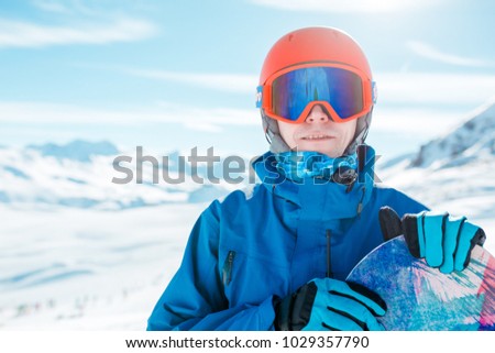Portrait of sportive man in helmet looking at camera with snowboard on background of snowy hill