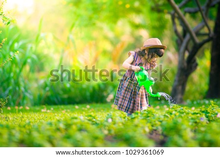 Asian little child girl pouring water on the trees. kid helps to care for the plants with a watering can in the garden. Royalty-Free Stock Photo #1029361069