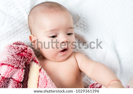 Beautiful happy small baby girl lying in bed and looking with smile. Closeup portrait