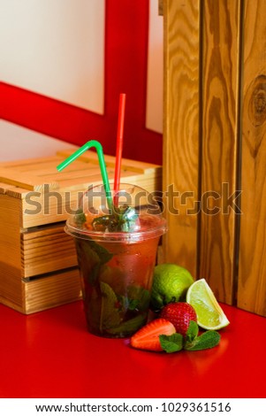 Strawberry Mojito with mint in a plastic cup with straws on a wooden table