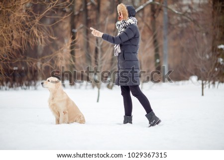 Picture of girl in black jacket training dog in snowy park