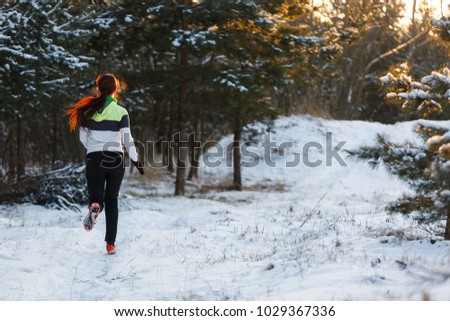 Image from back of athlete in sneakers on morning run against background of trees in winter