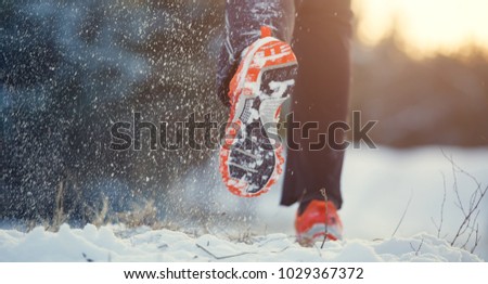 Image from back of running man in sneakers in sports clothes on snow