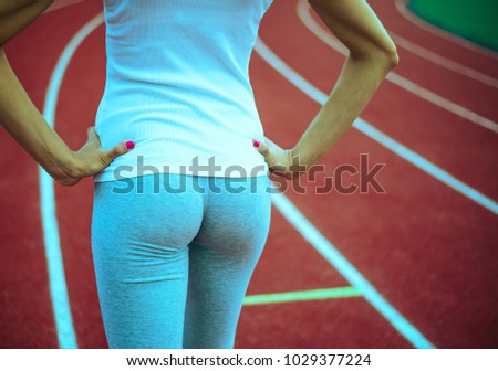 Close up. Back view. Young girl legs in stylish sneakers back side on a red race track of a stadium with white lane lines on background. Unrecognizable photo with copy space for inscription or objects