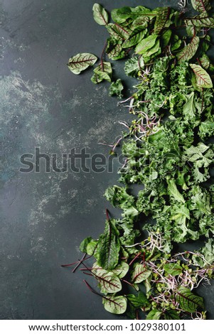 Green salad mix for salad or smoothie with kale, young beetroot leaves, sprouts, over dark texture surface. Top view, space. Food background.