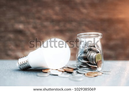 Energy saving LED BULB ECONOMY and Environment.Save the money.Business and technology concept.Coins in the glass on tile table desk with sunshine and brick background.