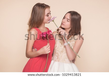 Two cheerful girls on a beige background with gerbera flowers, sniff, fragrance. Best friends, fun. A smiling woman.