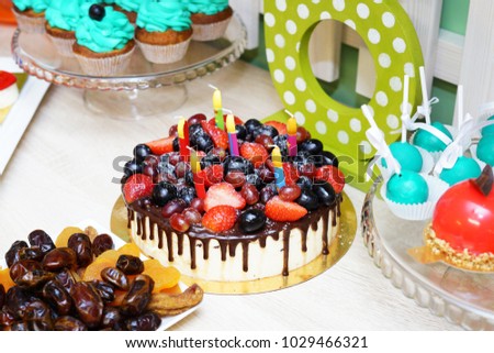 Festive Birthday cake with fresh berries, fruit and streaks of chocolate on a light background and candles on white table
