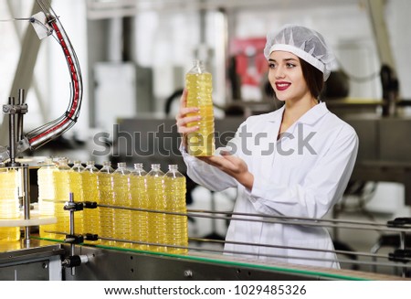 line of food production of refined sunflower oil. Girl worker at a factory on a conveyor background with bottles of vegetable oil.