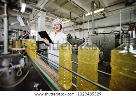 beautiful young girl is making notes on a sheet of paper on the background of a line on food production of sunflower oil.