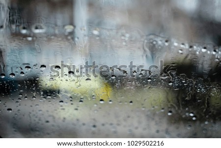 Car windshield with rain drops during falling rain  Shallow depth of field with focus on center of the windshield and urban background
