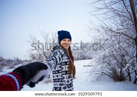 Follow me. Attractive young woman in hat holding hand of her boyfriend and walking in winter park