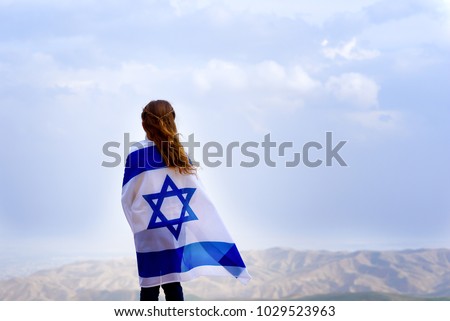 Little patriot jewish girl standing and  enjoying great view on the sky, valley and mountains with the flag of Israel wrapped around her. Memorial day-Yom Hazikaron and Yom Ha'atzmaut concept.  Royalty-Free Stock Photo #1029523963
