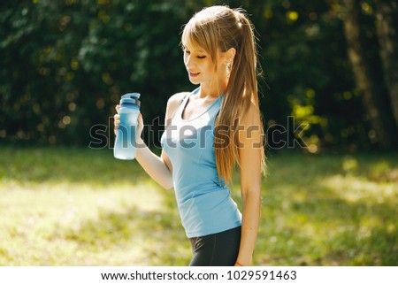 A young athletic girl stands in the summer park and drinks water