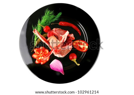 raw ribs on black plate with vegetables
