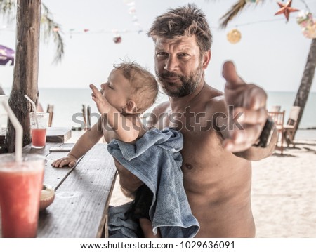  father and son sitting at beach bar counter and require the drinks, ocean and palms are behind them