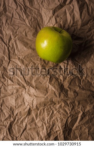 Green apple on wrinkled brown paper darkly lit in shadow