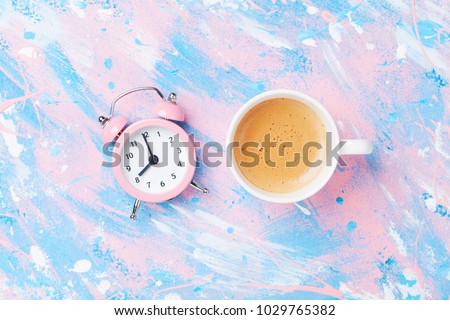 Morning cup of coffee and alarm clock on colorful working desk top view in flat lay style. Punchy pastel background. Royalty-Free Stock Photo #1029765382