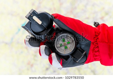 conceptual photo - search for missing tourists in the mountains in winter - a hand in the glove holds a compass on the background of the map