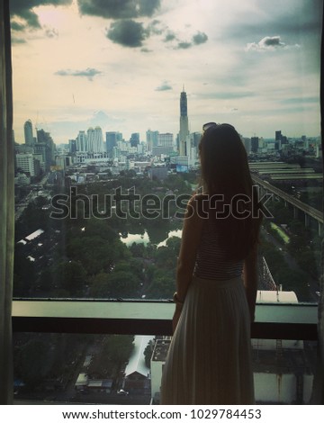 A woman with long hair at the window, she is looking outside city view with high building background in Bangkok Thailand.