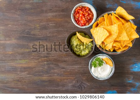Snack for a party, chips with a tortilla, nachos with sauces: salsa with tomatoes, sour cream and guacamole. Mexican food. Dark background. Top view. Copy space.