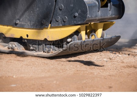 Manual road repair vibrating machine being pushed by a worker during road construction work on gravel road curbs. Road repairing in city. Heavy machinery 