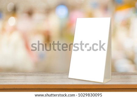Empty brown wooden table and Coffee shop interior with Mock up Menu frame in Bar restaurant ,Stand for booklets with white sheets of paper acrylic tent card on cafeteria blurred background