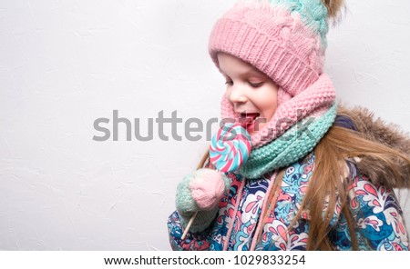 smiling girl with lollipop in winter clothes on white background
